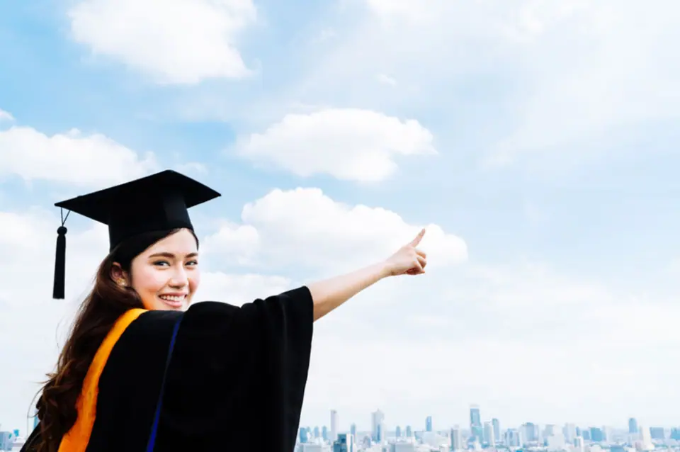 Graduate in cap and gown pointing towards a city skyline